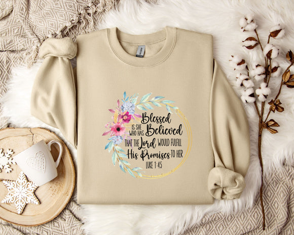 A beige sweatshirt with a floral design and text printed on it, along with a coffee mug and some white flowers on a bed.