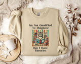 a beige sweatshirt with a humorous text and an illustration of a cat surrounded by books, placed on a bed with a white blanket and a mug.
