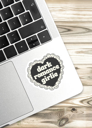 A laptop with a heart-shaped sticker on the palm rest, placed on a wooden surface.
