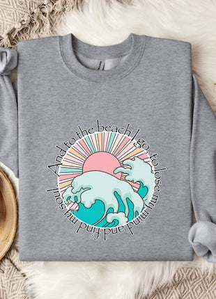a gray sweatshirt with a colorful graphic design, a mug, and some cotton balls on a bed with a blanket.