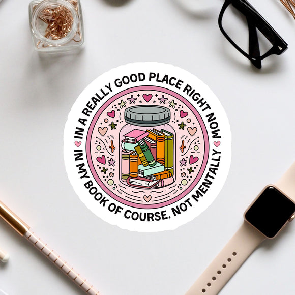A sticker with a book inside a jar surrounded by various decorative elements, along with a pair of glasses, a pen, and a watch on a white surface.